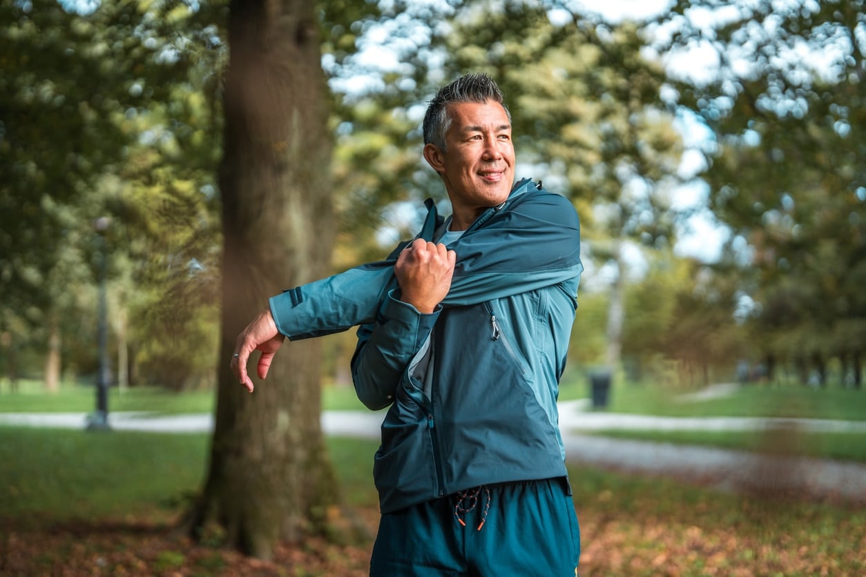 An Asian man in his mid-adult years practices outdoor fitness by stretching in a public park.