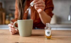 Woman pouring organic cannabis oil into her morning tea, promoting relaxation and wellness in a cozy kitchen setting