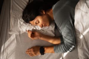 Young adult woman sleeping peacefully in bed with a smartwatch on her wrist, tracking sleep and health